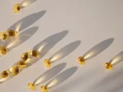 Gula kapslar med d-vitamin och magnesium sprids ut på en ljus yta, med långa skuggor som skapas av solljuset.
