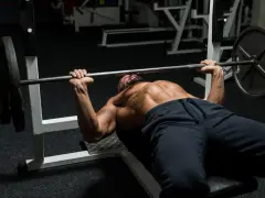 Man med skägg och synliga muskler utför bänkpress som en del av sitt starting strength program.
