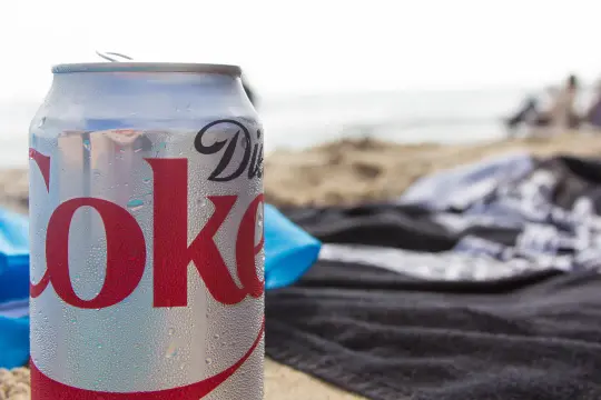 En burk Diet Coke på stranden, perfekt för den som vill undvika socker och hantera diabetes. Sukralos i drycken gör den till ett sockerfritt alternativ.