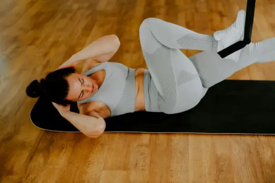 Kvinna gör situps på en matta, med fötterna fästa i ett träningsband. Hon jobbar hårt för att få bort magen på 2 veckor.