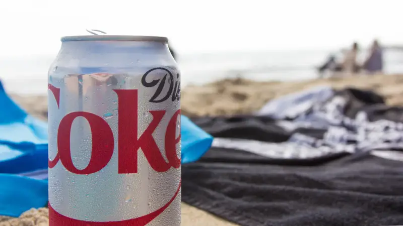En burk Diet Coke på stranden, perfekt för den som vill undvika socker och hantera diabetes. Sukralos i drycken gör den till ett sockerfritt alternativ.